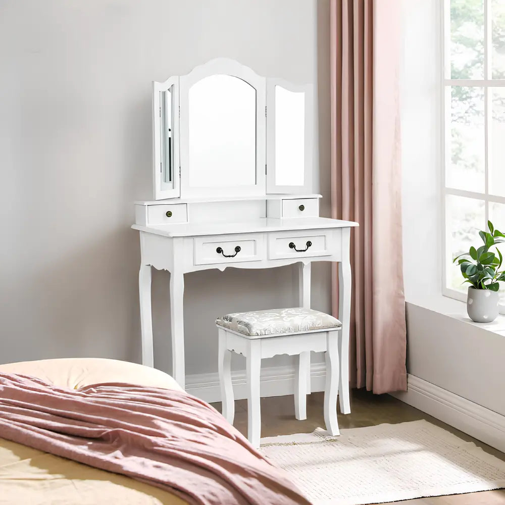 Coiffeuse blanche CELERA avec miroir triptyque et tabouret, éclairée par la lumière naturelle d’une chambre élégante
